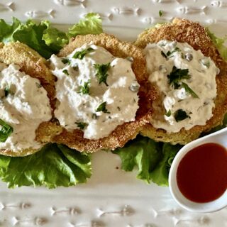 3 Fried green tomatoes topped with crab salad and a side of red sauce.