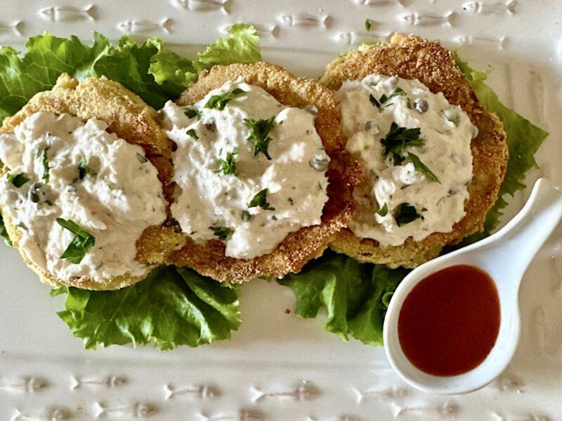3 Fried green tomatoes topped with crab salad and a side of red sauce.