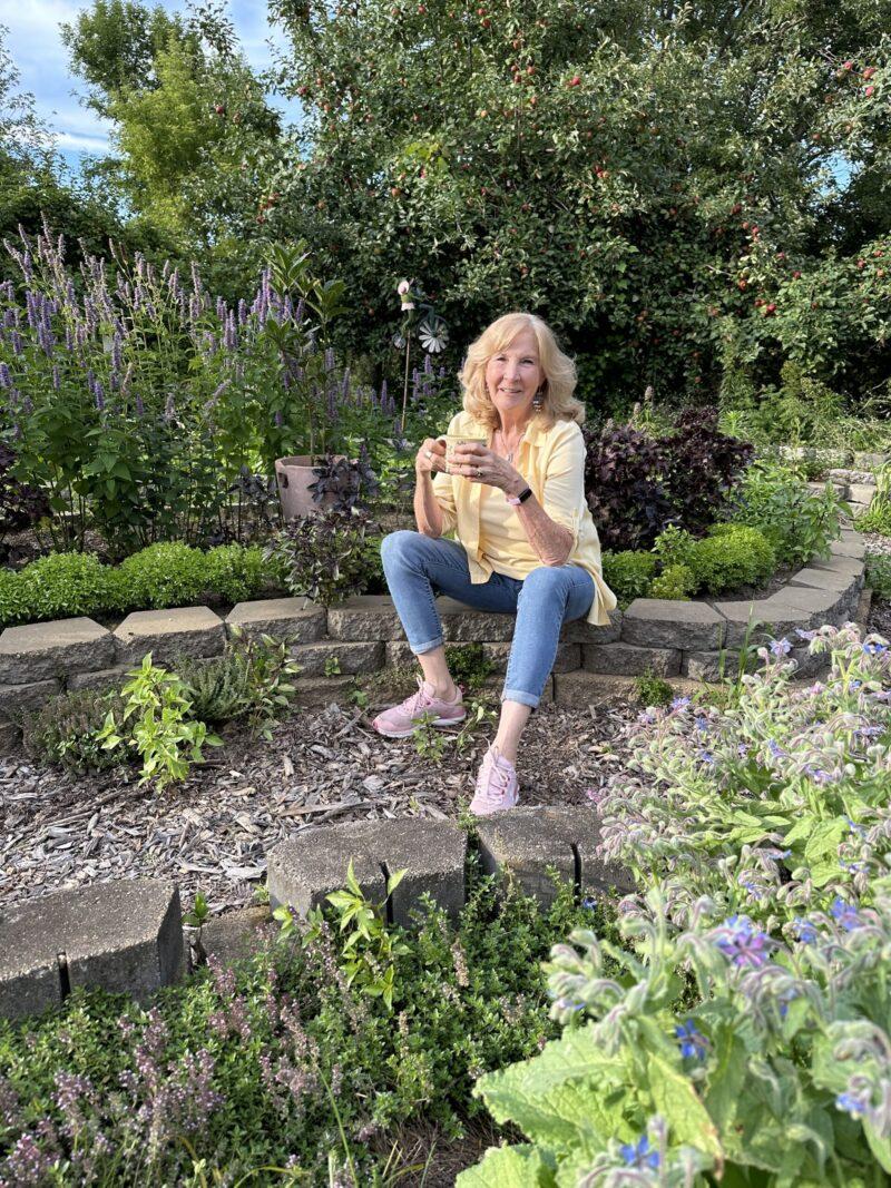 Dorothy Stainbrook in the herb garden with a cup of wellness tea