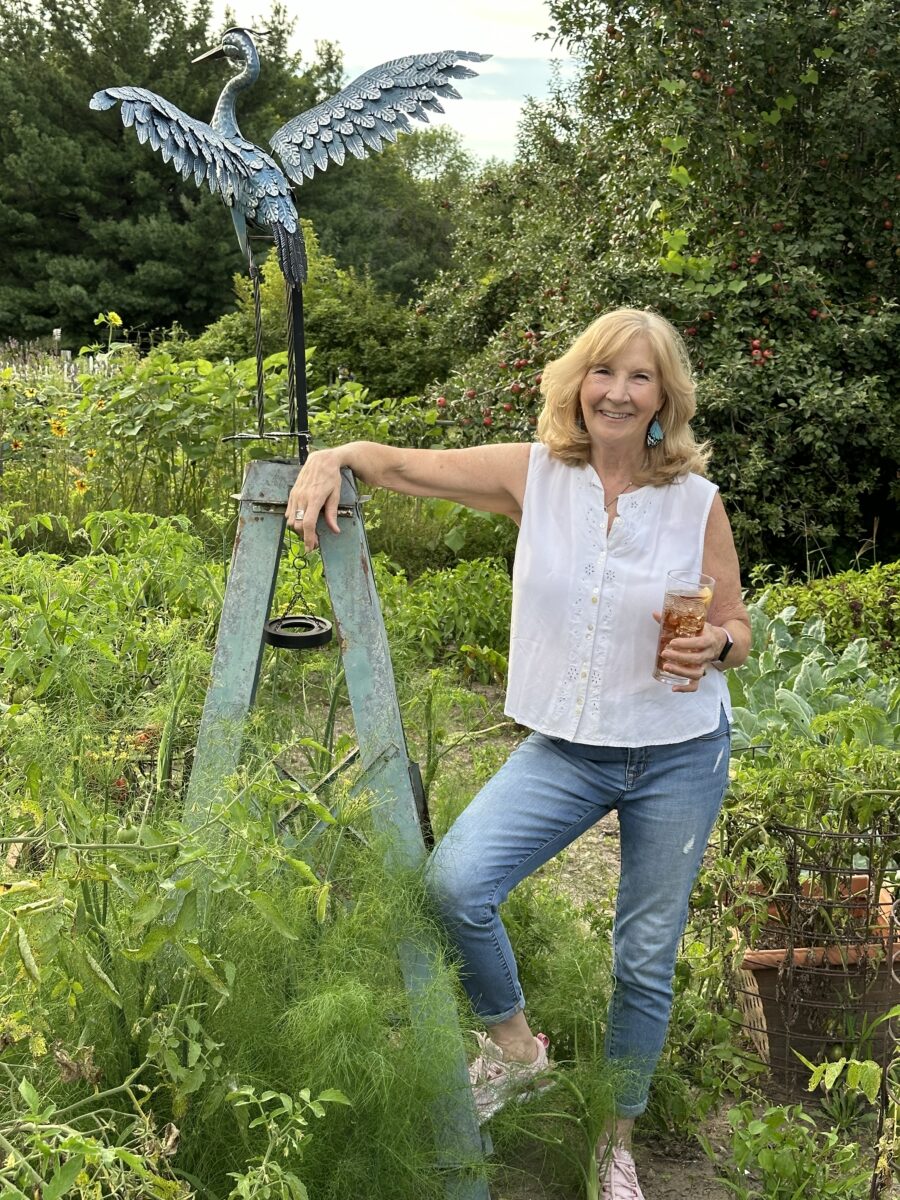 Dorothy Stainbrook in the Italian summer garden holding wellness tea in front of bird statue