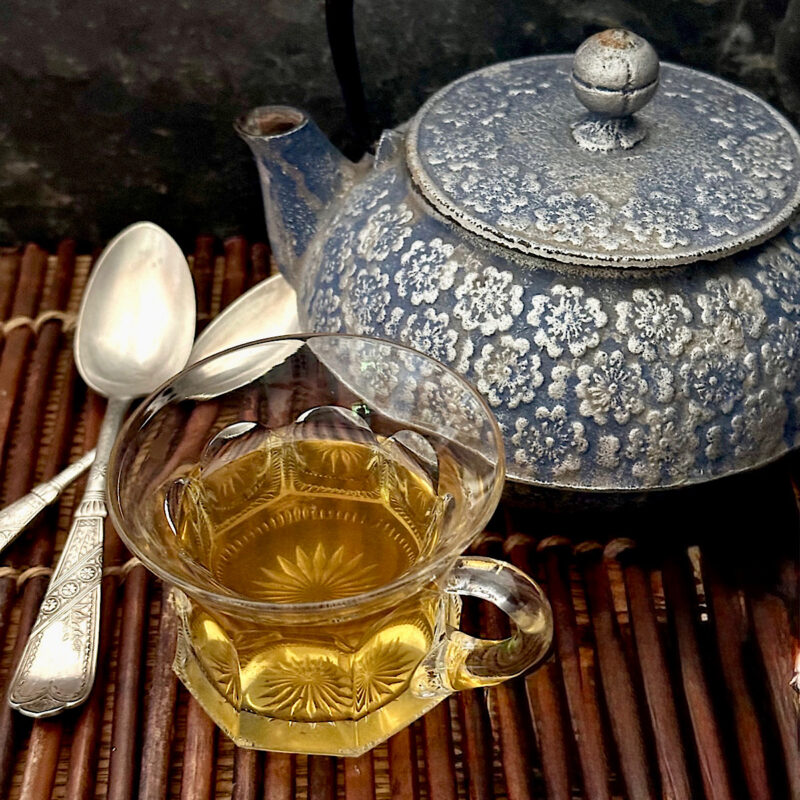 Spruce tip tea with blue teapot and 2 spoons.