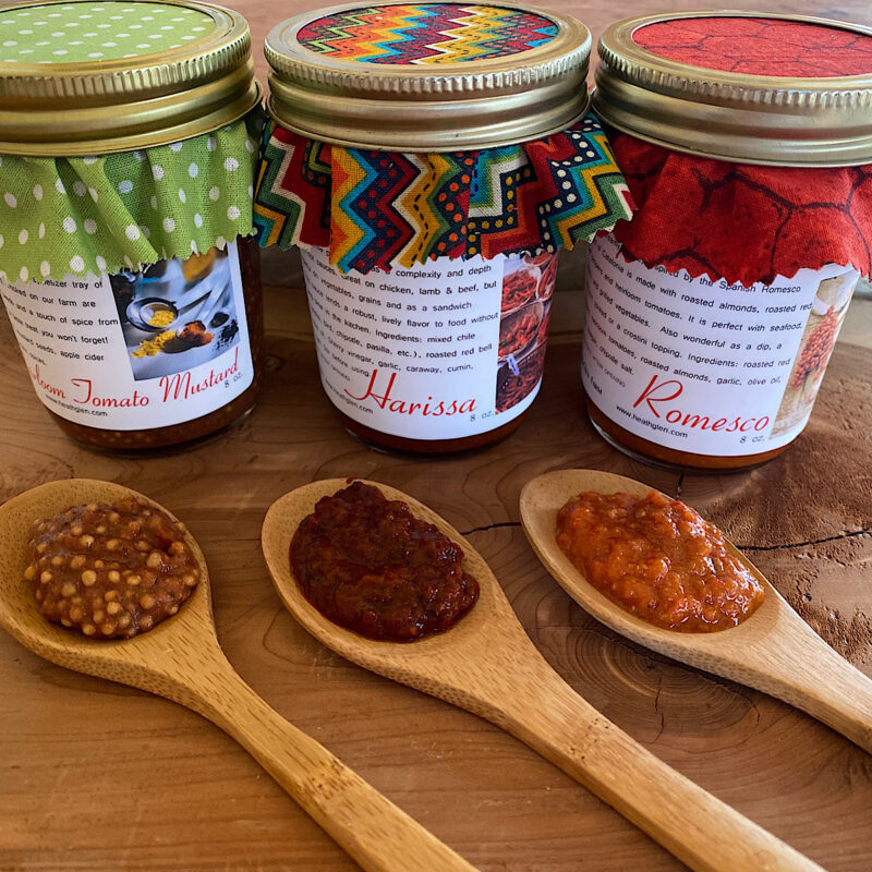 3 Sauces from HeathGlen: Tomato Mustard, Harissa and Romesco with spoonfuls of each sauce in front of associated jar.