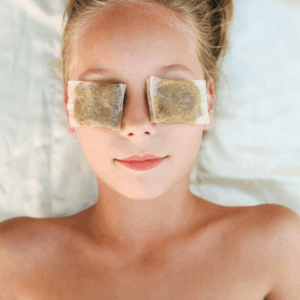 Image of green tea bags being used to help woman relieve puffy eyes.