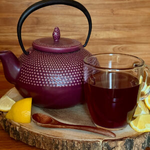 Brewed Lapsang Souchong looseleaf tea (Builders Brew). A purple teapot with brewed cup on a round of wood with lemon wedges on the side.