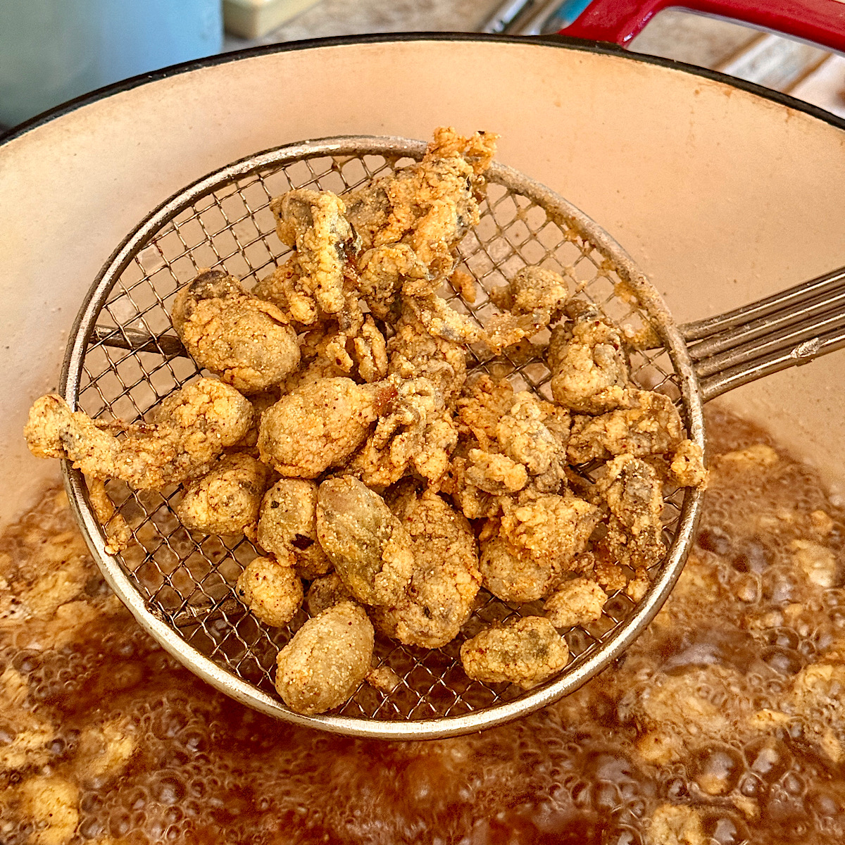 Large slotted spoon of breaded oysters after frying in hot oil for 2-3 minutes.