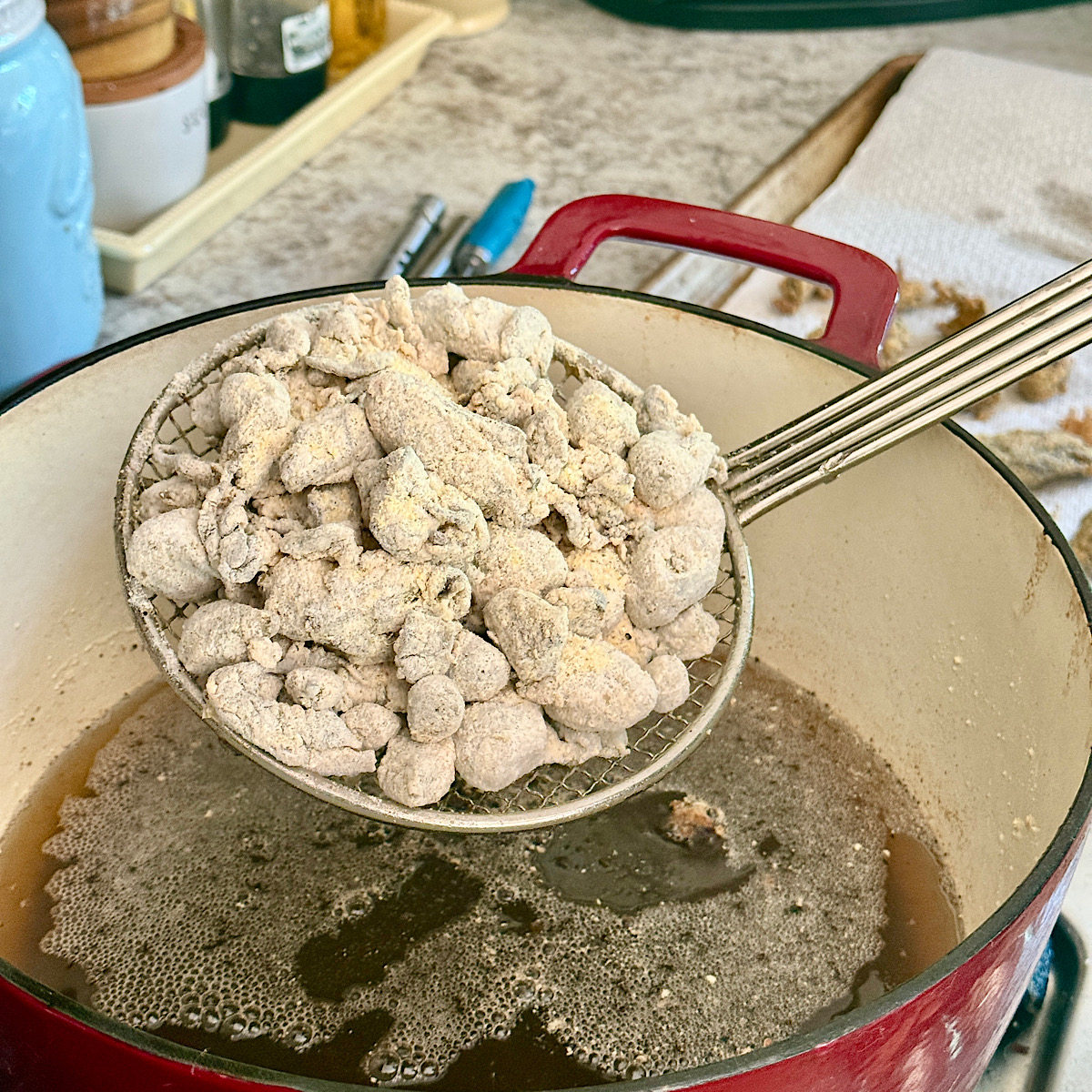 Breaded oysters being placed in a cast iron dutch oven with oil heated to 360 degrees F.