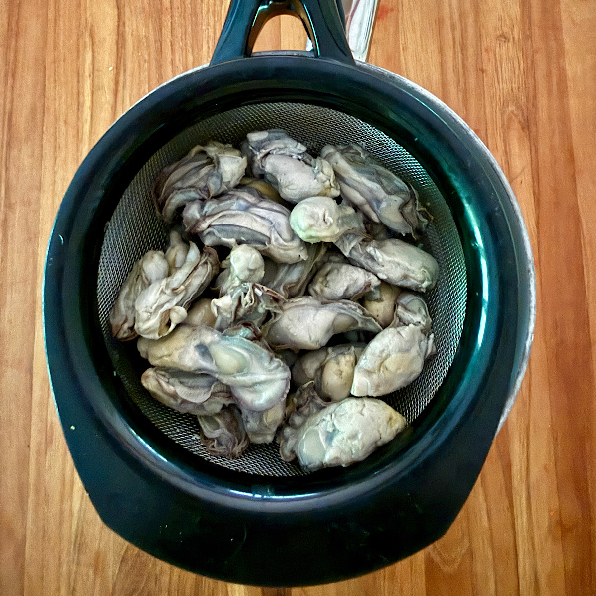Canned oysters in a sieve over a bowl to drain liquid before deep frying oysters in breading for an Oyster Po Boy sandwich.