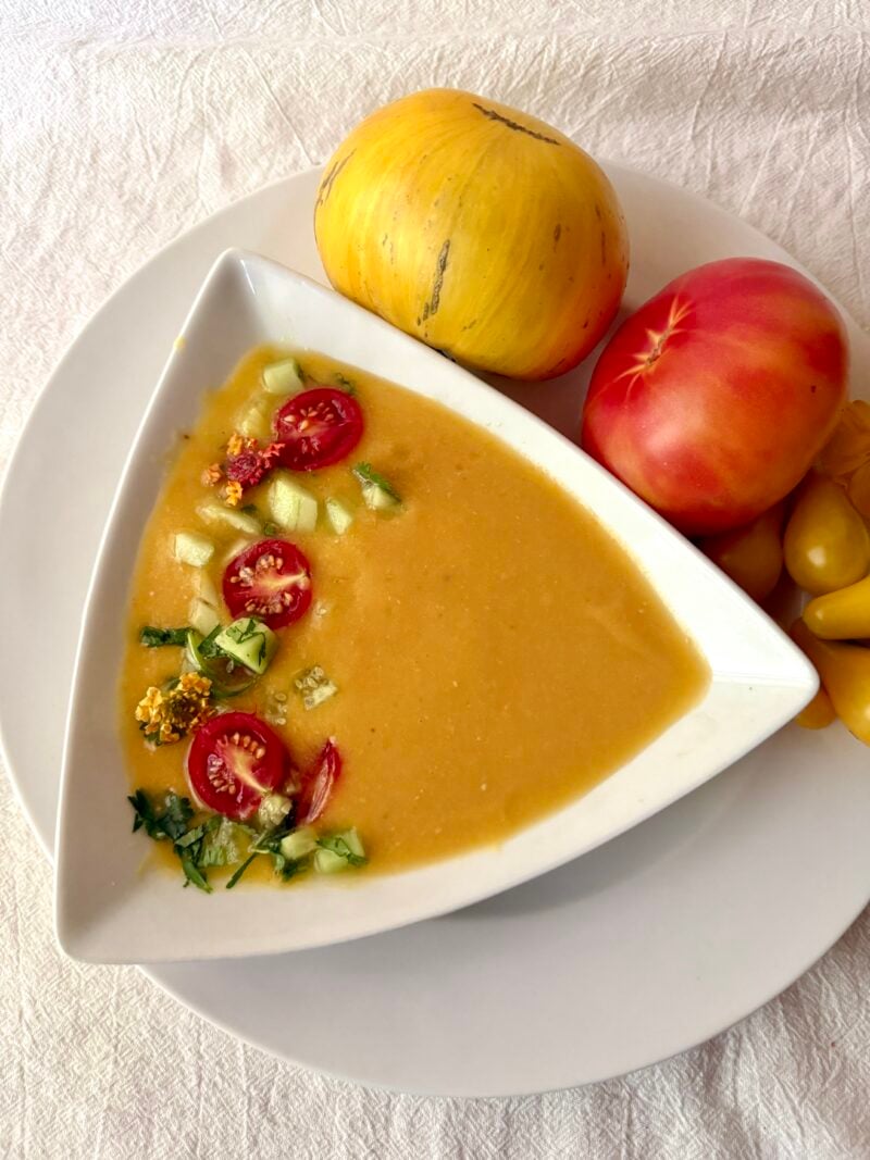 Yellow heirloom tomato gazpacho using heirloom tomatoes from HeathGlen Farm. Includes varieties called Pork Chop, Oaxaca Gold, and Yellow Pear. Garnished with red cherry tomatoes, chopped cucumbers and cilantro.