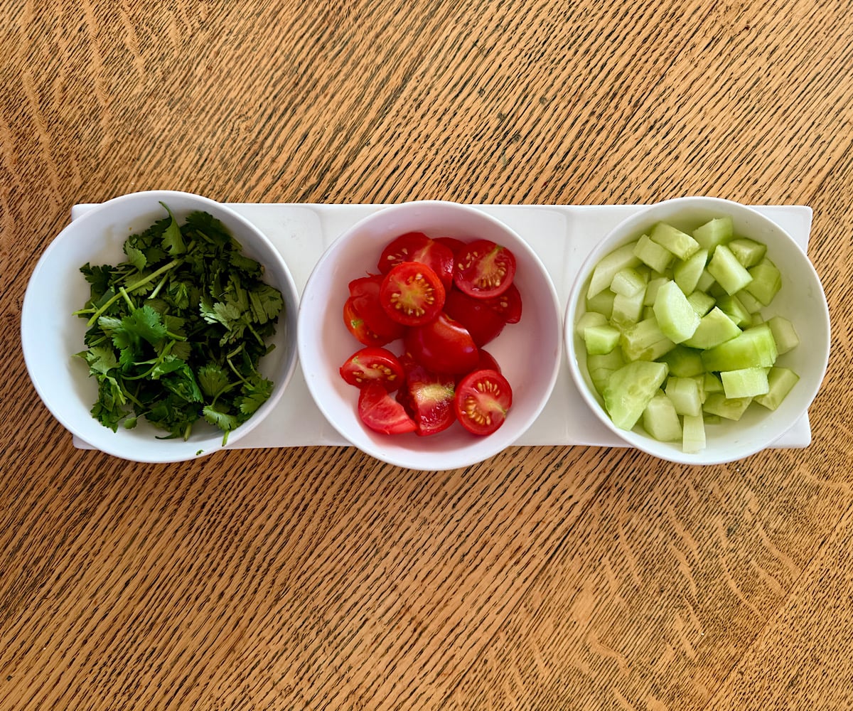 Side accompaniments and garnishes for yellow gazpacho, including chopped cucumbers, sliced cherry tomatoes, and minced cilantro.