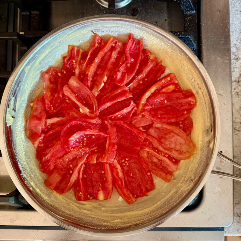 Fresh Roma tomatoes arranged on top of a layer of butter and sugar in a stainless steel pan in order to be caramelized for a tomato tarte tatin.