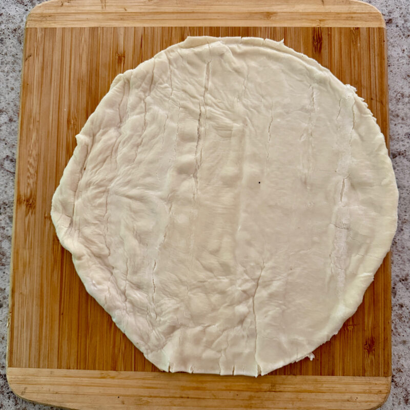 Store-bought puff pastry cut into a round to be placed on carmelized tomatoes for a tomato tarte tatin.