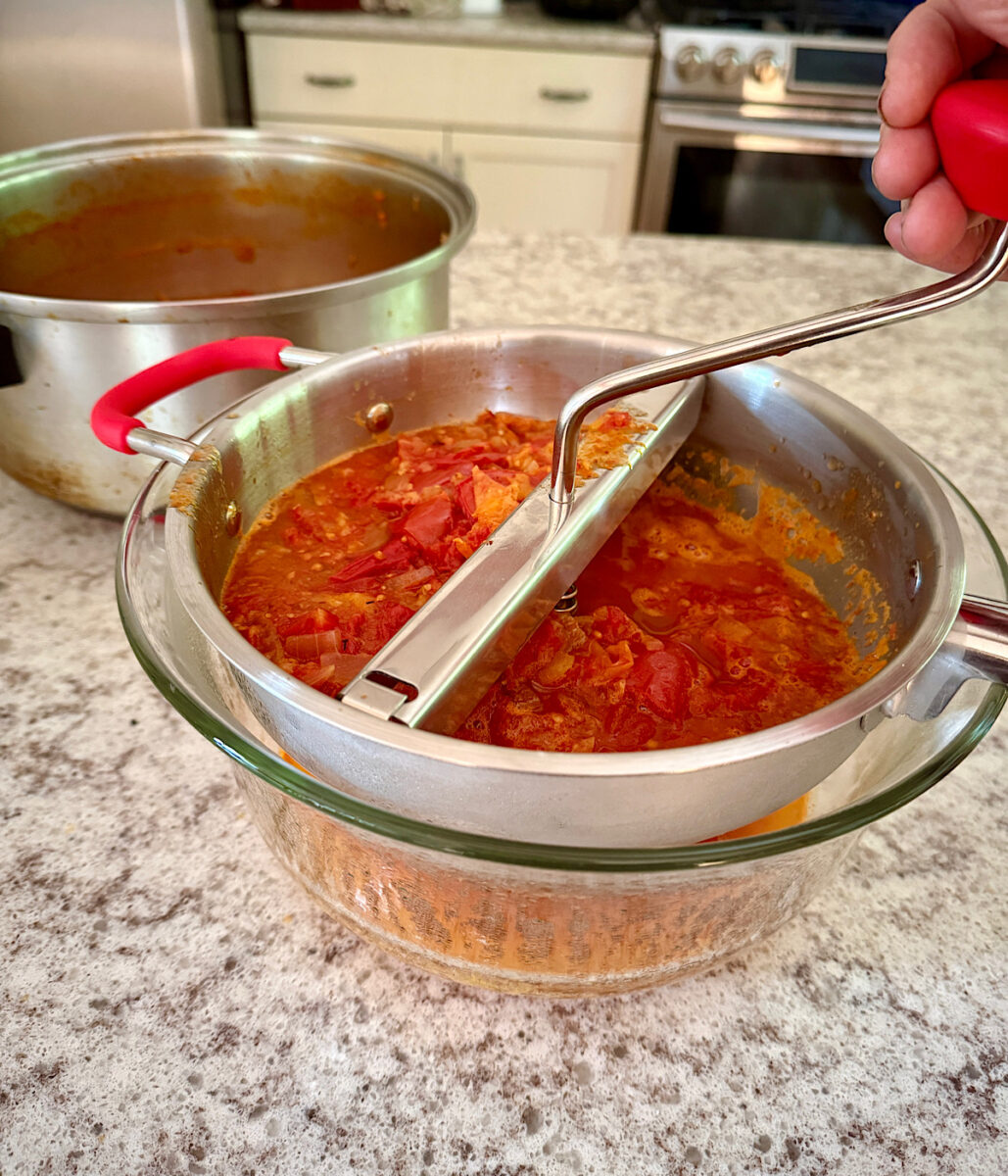 Using a hand-held food mill to remove skins and seeds from a cooked heirloom tomato sauce.
